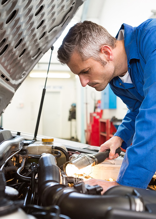 mechanic inspecting car engine with flashlight