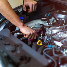 close up of hands reaching into engine of car